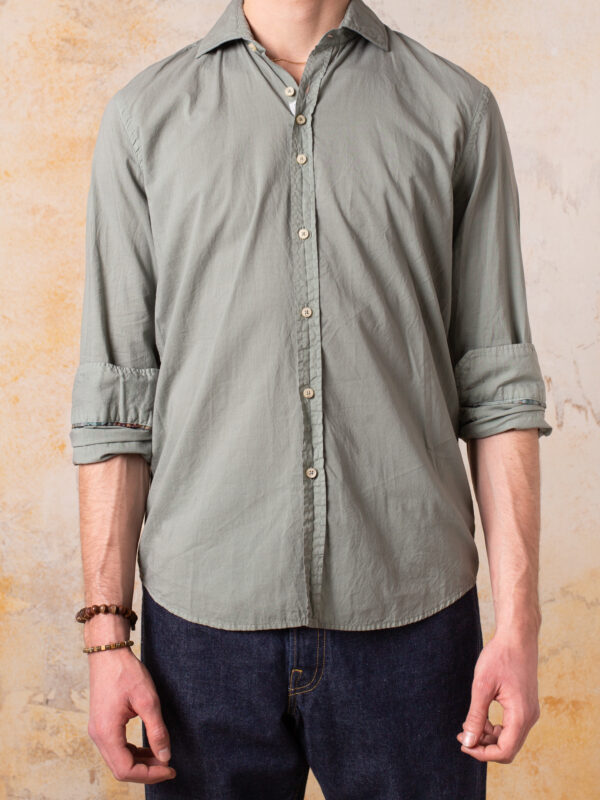 Camisa Bjovuit Cadaqués 06 – Proceso Artesanal Tintado Una camisa confeccionada en 100% algodón extrafino de alta calidad, con un diseño sofisticado que destaca por su proceso artesanal de tintado, logrando una tonalidad verde única y una textura excepcional. 100% Algodón extrafino, ligero y transpirable para una comodidad inigualable. Diseñada y fabricada en Barcelona, reflejando el equilibrio entre tradición y modernidad. Color verde oliva exclusivo, obtenido mediante un proceso artesanal que realza la textura natural del tejido. Corte sofisticado y versátil, perfecto para un look elegante y relajado. Detalles cuidados, que elevan su estilo y exclusividad.